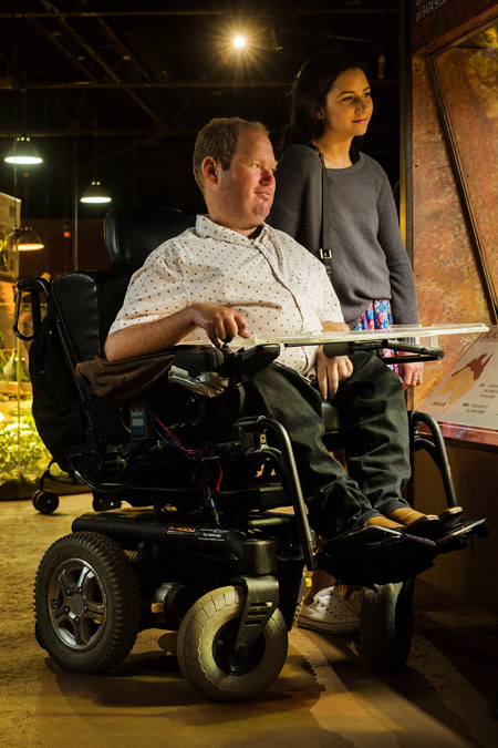 A man in a wheelchair and his companion visit exhibits at a museum.