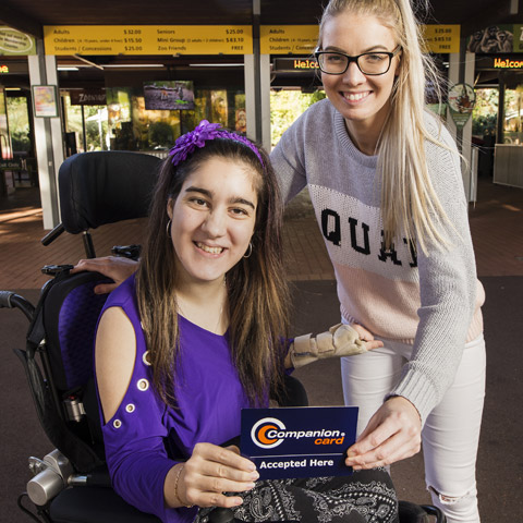 Two young women holding a sign which reads Companion Card Accepted Here.